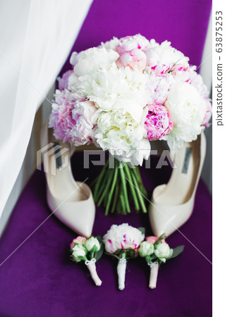 Pair of elegant and stylish bridal shoes with a bouquet with roses and other flowers 63875253