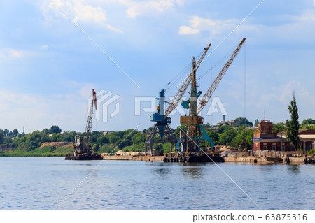 Heavy cranes in cargo port on the riverbank 63875316