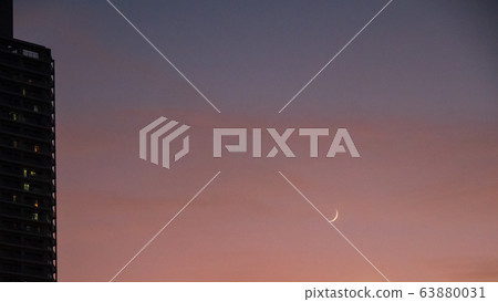 A red sky in the evening with a small crescent moon low in the sky 63880031