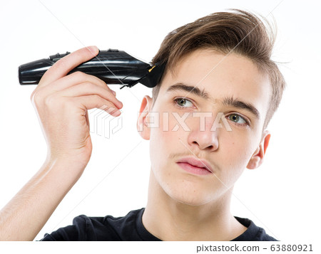 Teenage boy cuts his own hair with an electric 63880921