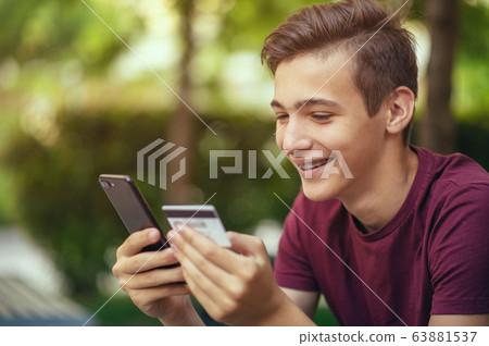 Teenage boy with a credit card and phone makes 63881537
