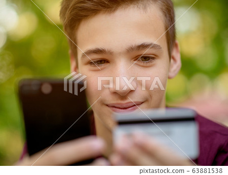 Teenage boy with a credit card and phone makes 63881538