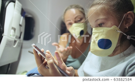 Family woman and child baby travel tourist caucasian at plane aircraft with wearing protective medical mask. Use smartphone mobile. Covid-19 Family woman and child baby travel tourist caucasian at plane aircraft with wearing protective medical mask. Use smartphone mobile. Covid-19 63882584
