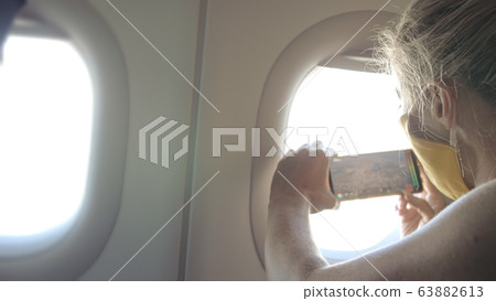 Woman travel caucasian at plane with wearing protective medical mask. Girl tourist at aircraft with respirator, make photo video at smartphone mobile. Woman travel caucasian at plane with wearing protective medical mask. Girl tourist at aircraft with respirator, make photo video at smartphone mobile. 63882613