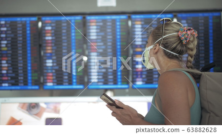Woman caucasian at Suvarnabhumi Airport with wearing protective medical mask. Flight Information Board. Use smartphone mobile. Sars-cov-2 covid-19. 63882628