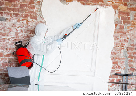 Coronavirus Pandemic. A disinfector in a protective suit and mask sprays disinfectants in the house or office Coronavirus Pandemic. A disinfector in a protective suit and mask sprays disinfectants in the house or office 63885284