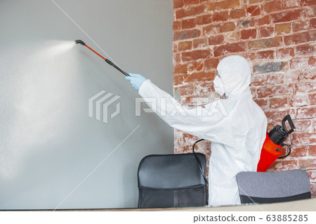 Coronavirus Pandemic. A disinfector in a protective suit and mask sprays disinfectants in the house or office Coronavirus Pandemic. A disinfector in a protective suit and mask sprays disinfectants in the house or office 63885285