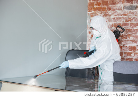 Coronavirus Pandemic. A disinfector in a protective suit and mask sprays disinfectants in the house or office Coronavirus Pandemic. A disinfector in a protective suit and mask sprays disinfectants in the house or office 63885287