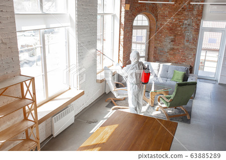 Coronavirus Pandemic. A disinfector in a protective suit and mask sprays disinfectants in the house or office Coronavirus Pandemic. A disinfector in a protective suit and mask sprays disinfectants in the house or office 63885289