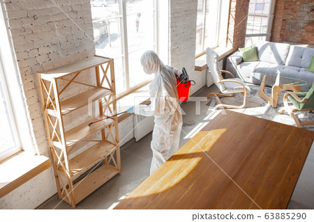 Coronavirus Pandemic. A disinfector in a protective suit and mask sprays disinfectants in the house or office Coronavirus Pandemic. A disinfector in a protective suit and mask sprays disinfectants in the house or office 63885290
