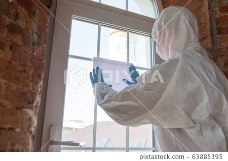 Coronavirus Pandemic. A disinfector in a protective suit and mask making a warning sign, copyspace 63885395