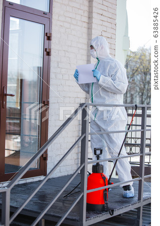 Coronavirus Pandemic. A disinfector in a protective suit and mask sprays disinfectants in the house or office 63885426