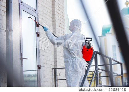 Coronavirus Pandemic. A disinfector in a protective suit and mask sprays disinfectants in the house or office Coronavirus Pandemic. A disinfector in a protective suit and mask sprays disinfectants in the house or office 63885438