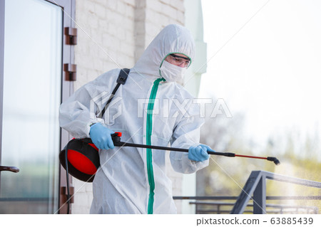 Coronavirus Pandemic. A disinfector in a protective suit and mask sprays disinfectants in the house or office 63885439