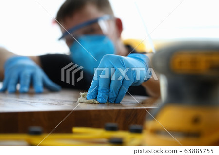 Carpenter in gloves cleans polishes wooden surface 63885755