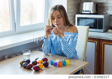 Holidays, handmade and creation concept - Happy young woman draws on Easter egg. Holidays, handmade and creation concept - Happy young woman draws on Easter egg. 63886327