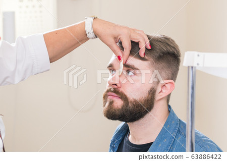 Medicine, health, ophthalmology concept - Ophthalmologist examines patient's eyes. Medicine, health, ophthalmology concept - Ophthalmologist examines patient's eyes. 63886422