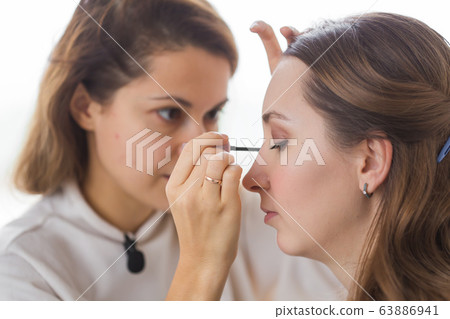 Beauty and cosmetics concept - Makeup artist doing professional make up of young woman Beauty and cosmetics concept - Makeup artist doing professional make up of young woman 63886941