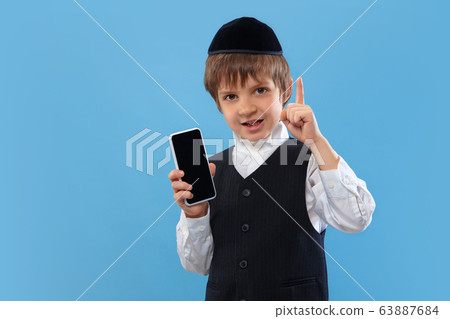 Portrait of a young orthodox jewish boy isolated on blue studio background, meeting the Passover Portrait of a young orthodox jewish boy isolated on blue studio background, meeting the Passover 63887684