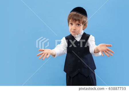 Portrait of a young orthodox jewish boy isolated on blue studio background, meeting the Passover Portrait of a young orthodox jewish boy isolated on blue studio background, meeting the Passover 63887733