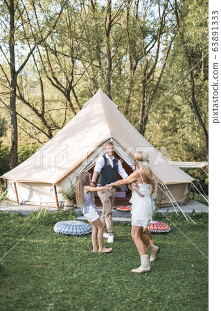 Happy family: mother, father, two children daughters on nature on sunset, dancing and having fun. Boho style, wigwam on the background Happy family: mother, father, two children daughters on nature on sunset, dancing and having fun. Boho style, wigwam on the background 63891333