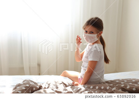 Girl in a respiratory mask sits in quarantine at home. 63892016
