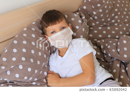 A boy in a respiratory mask sits in quarantine at home 63892042