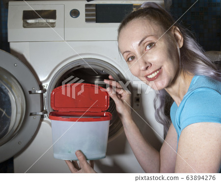 joyful woman in the background of a washing machine holds a box with washing gel in her hands, joyful woman in the background of a washing machine holds a box with washing gel in her hands, 63894276
