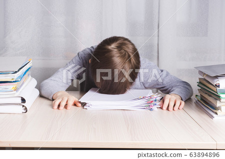 Tired schoolboy lying on the table clutching his Tired schoolboy lying on the table clutching his 63894896
