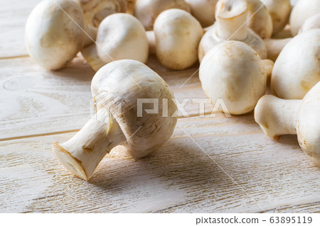 Close-up of whole raw fresh champignon on a white wooden table. Close-up of whole raw fresh champignon on a white wooden table. 63895119