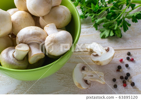 Whole raw fresh champignons in a green bowl near bunch of parsley on a wooden table. Whole raw fresh champignons in a green bowl near bunch of parsley on a wooden table. 63895120