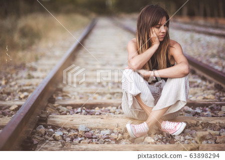 Sad young woman sitting on the railway. Sad young woman sitting on the railway. 63898294
