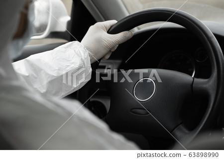 Man in protective suit, medical mask and rubber gloves for protect from bacteria and virus is driving a car. Protective mask while quarantine, world pandemic, covid 19, coronavirus, infection. 63898990