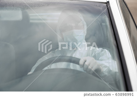 Man in protective suit, medical mask and rubber gloves for protect from bacteria and virus is driving a car. Protective mask while quarantine, world pandemic, covid 19, coronavirus, infection. 63898991