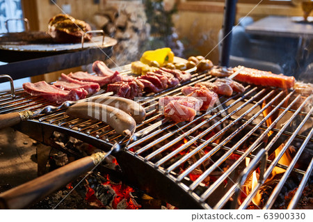 The meat is pickled on a lattice grill, ribs spread, a stake, Sausages, edges, chicken, naked flame, black pepper, a smoke, firewood, light reflections, close up 63900330