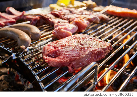 The meat is pickled on a lattice grill, ribs spread, a stake, Sausages, edges, chicken, naked flame, black pepper, a smoke, firewood, light reflections, close up The meat is pickled on a lattice grill, ribs spread, a stake, Sausages, edges, chicken, naked flame, black pepper, a smoke, firewood, light reflections, close up 63900335