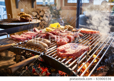 The meat is pickled on a lattice grill, ribs spread, a stake, Sausages, edges, chicken, naked flame, black pepper, a smoke, firewood, light reflections, close up The meat is pickled on a lattice grill, ribs spread, a stake, Sausages, edges, chicken, naked flame, black pepper, a smoke, firewood, light reflections, close up 63900336