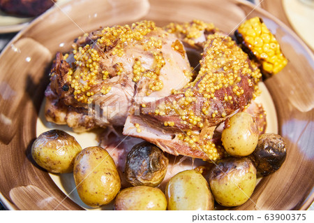 The big piece of the grilled stewed pork with mustard sauce lies on a plate with potatoes and corn, Juicy meat The big piece of the grilled stewed pork with mustard sauce lies on a plate with potatoes and corn, Juicy meat 63900375