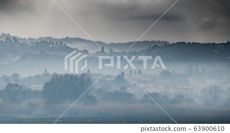 Fog over the city on a slope in cloudy weather, cypresses stick out, Corfu, Greece 63900610