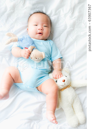 Portrait of a newborn Asian baby boy on the bed with a doll , Charming 63907367
