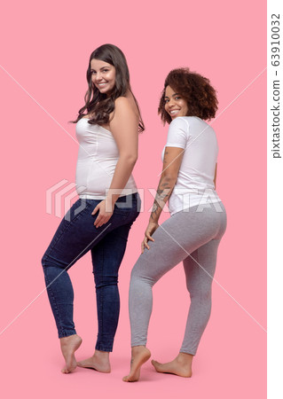 Two young cheerful women standing unfolded sideways and back. 63910032
