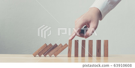 Hand stopping wooden domino business crisis effect 63910608