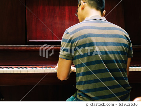 Asian young man playing piano at home Asian young man playing piano at home 63912636