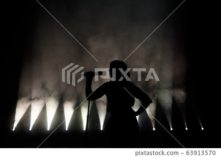 black silhouette of female singer with white spotlights in the background 63913570
