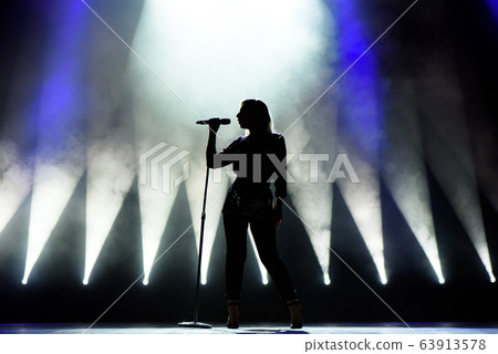 Silhouette of singer on stage. Dark background, smoke, spotlights. 63913578