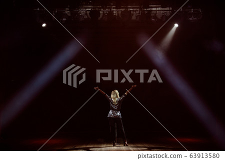 A young woman singer on stage during a concert view from the back. 63913580