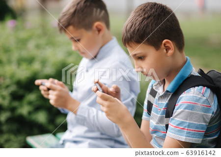 Two boy sitting on the bench and play online games. One boys with backpack. Young boys use their phones. Quarantine 63916142