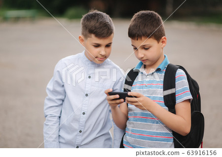 Two boys plays online games in quarantine. Young boys smile and use phone Two boys plays online games in quarantine. Young boys smile and use phone 63916156