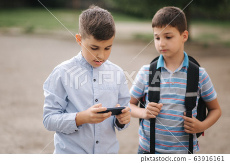 Two boys plays online games in quarantine. Young boys smile and use phone Two boys plays online games in quarantine. Young boys smile and use phone 63916161