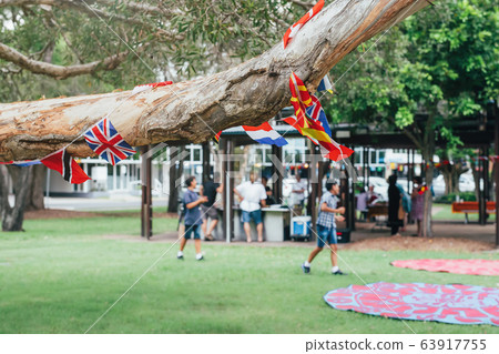 Flags of different countries in the tree branch with blured people in park doing barbecue together. Multicultural network, inclusivity concept Flags of different countries in the tree branch with blured people in park doing barbecue together. Multicultural network, inclusivity concept 63917755